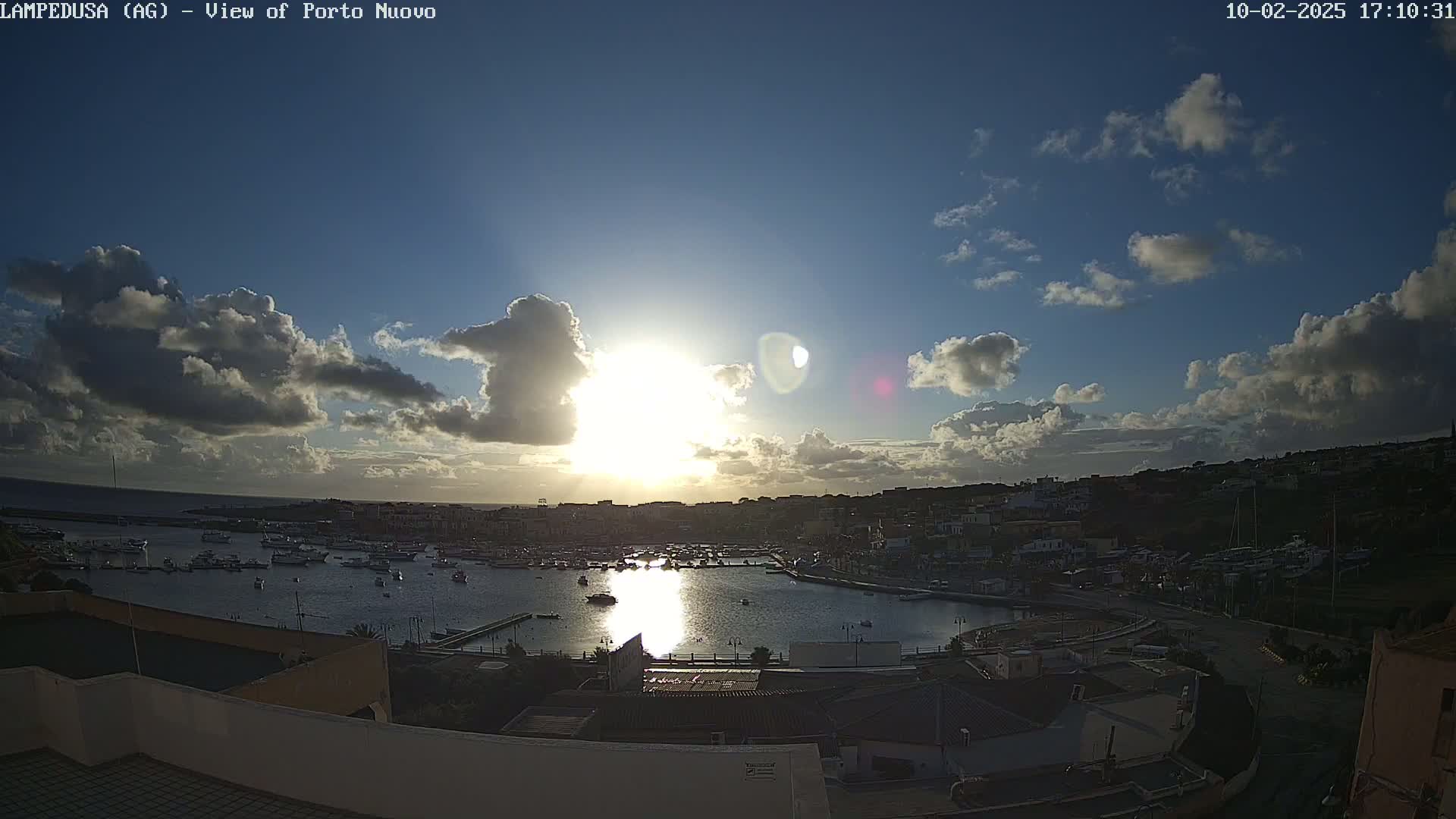 A partly cloudy sunset over a harbor filled with boats, viewed from an elevated position.