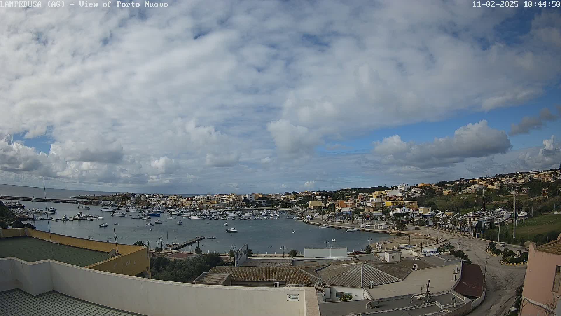 A partly cloudy day overlooks a harbor filled with numerous boats and surrounded by a town with low-rise buildings.