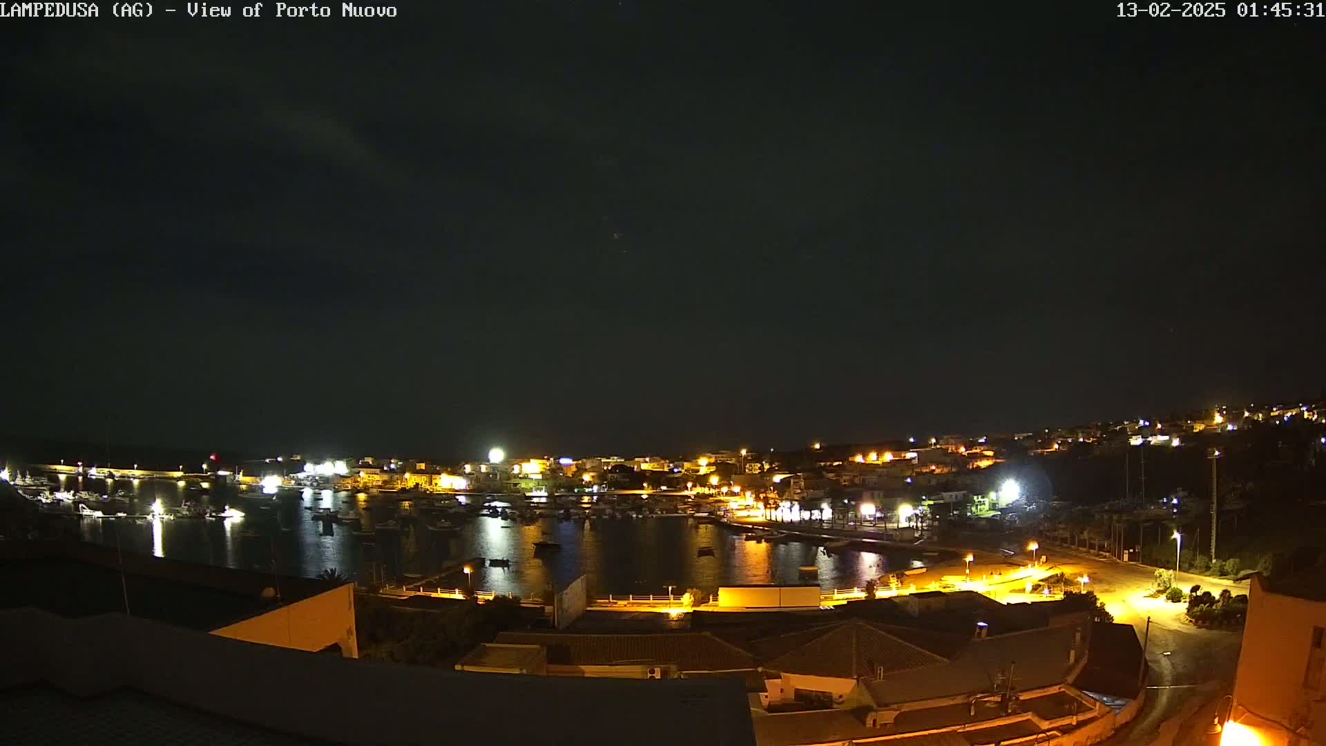 A nighttime, clear-sky view of a harbor filled with boats, surrounded by a town with illuminated buildings.