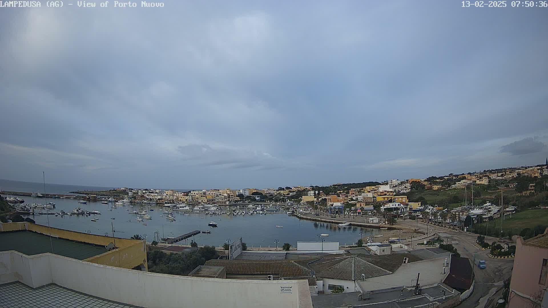 An overcast sky overlooks a harbor filled with boats and a town of low-rise buildings.