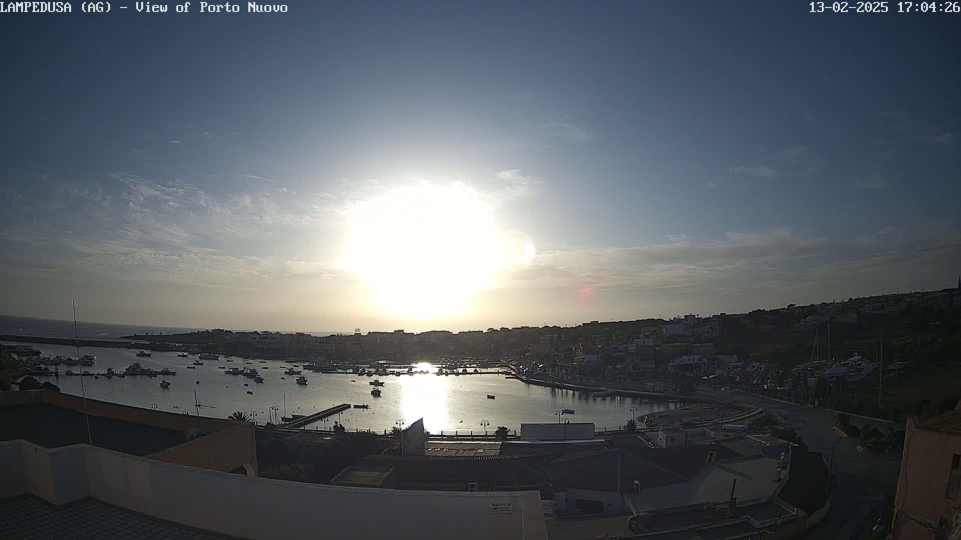 A harbor filled with boats is seen at sunset under a mostly clear sky.