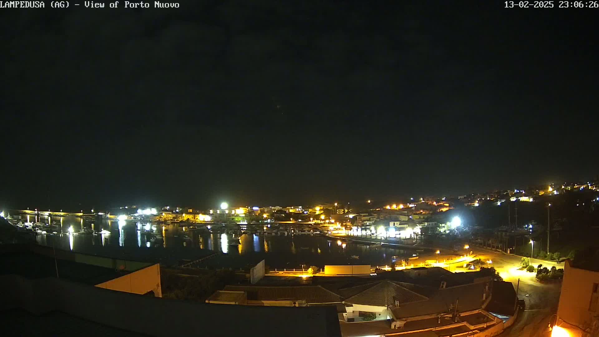 A nighttime, aerial view of a harbor town with boats in the water and lights illuminating buildings and streets under a clear, dark sky.