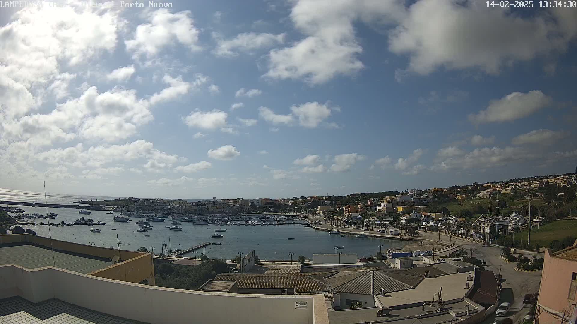 A partly sunny day overlooks a harbor filled with boats and a town nestled on a hillside.
