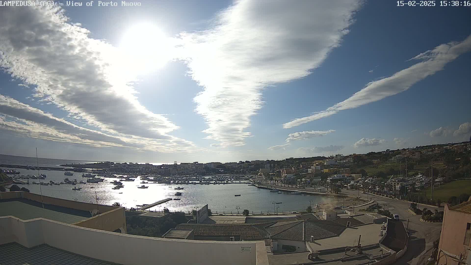 A partly sunny day with scattered clouds over a harbor filled with boats and a coastal town.