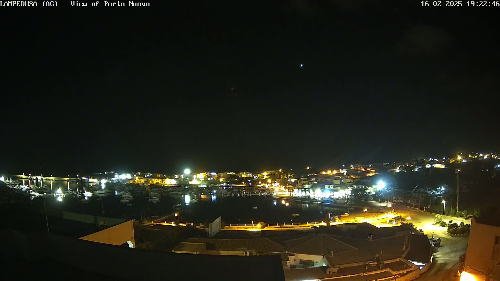 A nighttime, clear-sky view of a harbor town with boats docked and buildings lit up along the waterfront.