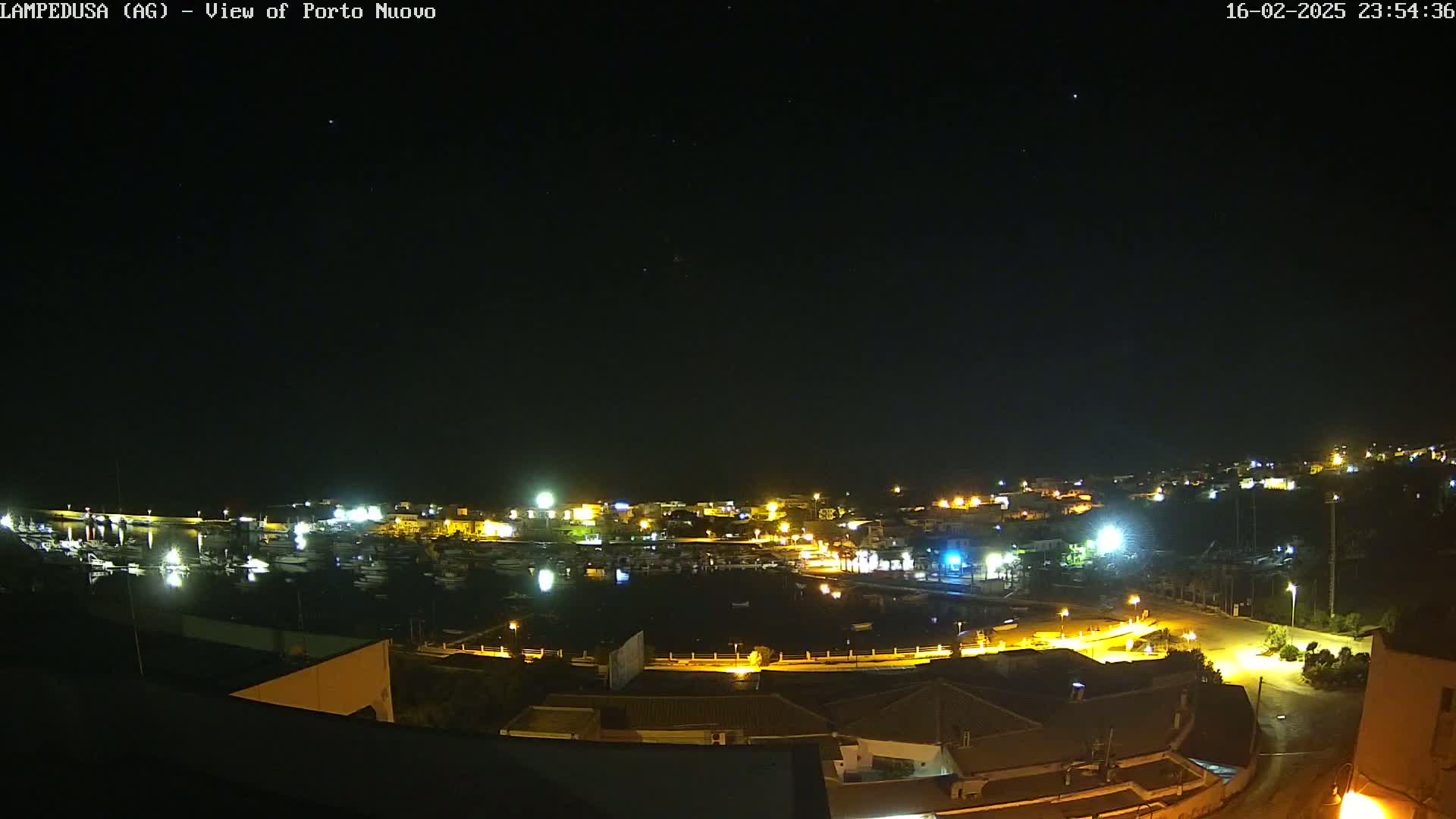 A nighttime, clear-sky view of a harbor town with brightly lit buildings and boats in the water.