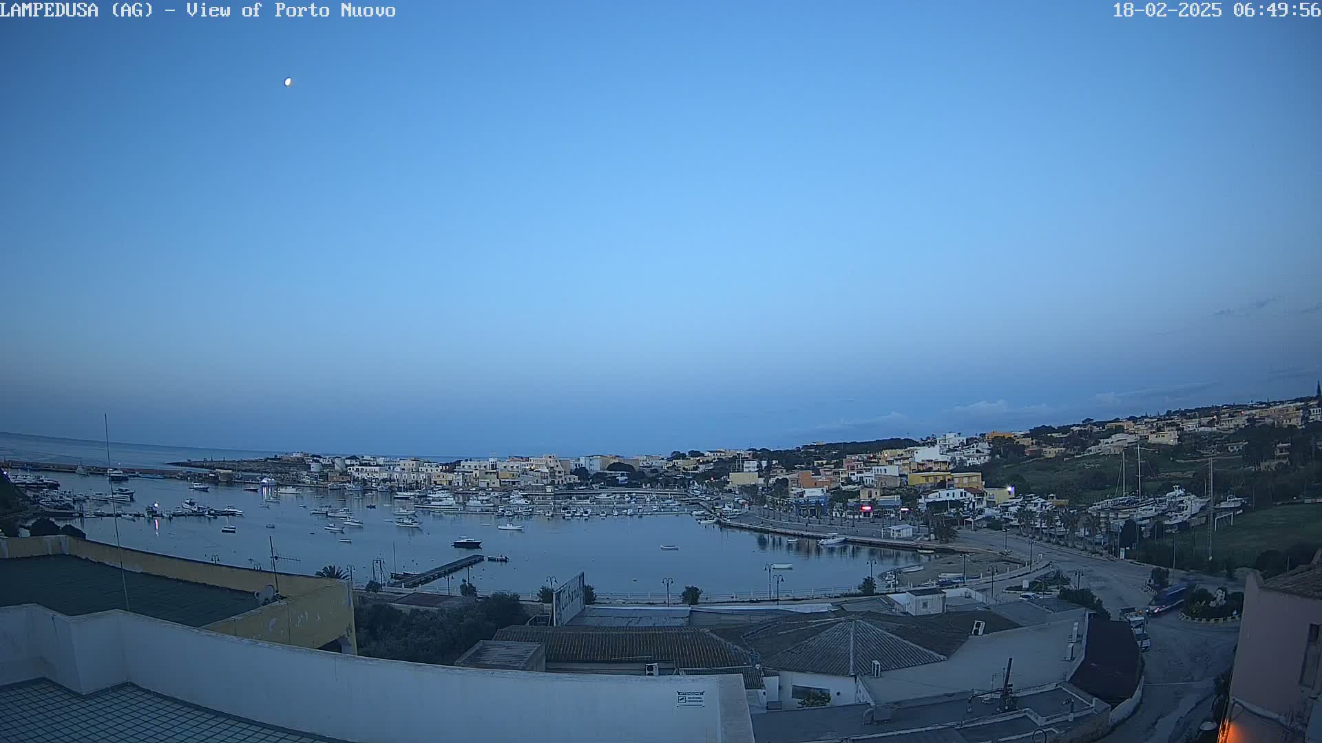 A harbor filled with boats is nestled in a town under a clear, twilight sky.