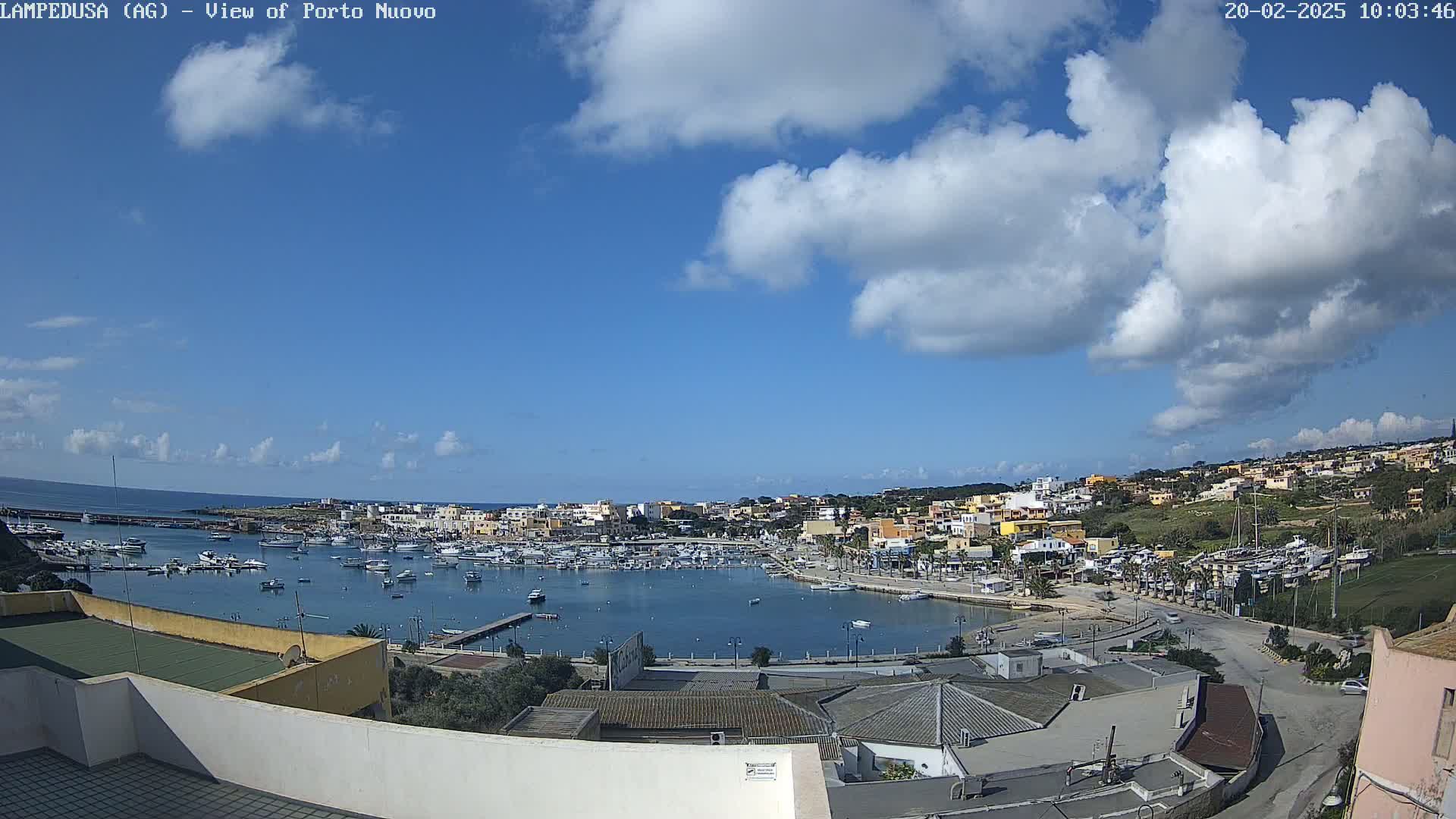 A partly cloudy day overlooking a harbor filled with boats and a town of low-rise buildings.