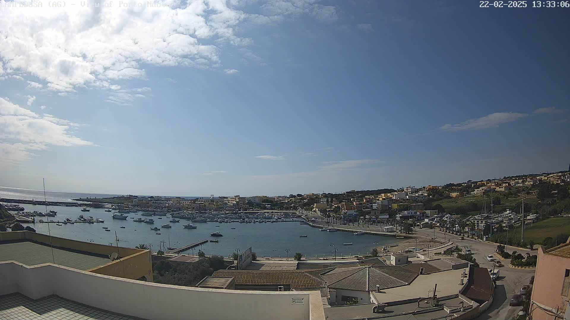 A partly cloudy day overlooking a harbor filled with boats and a town built on a hillside.