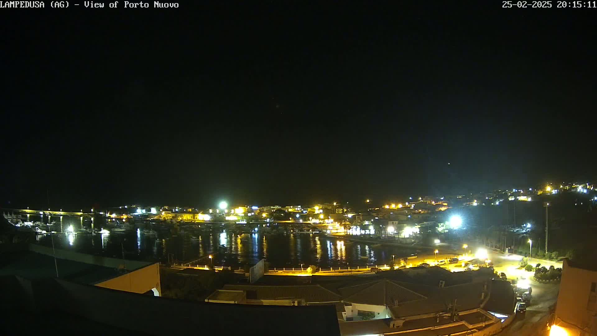 A nighttime, aerial view of a harbor town with many boats and buildings illuminated by artificial light.
