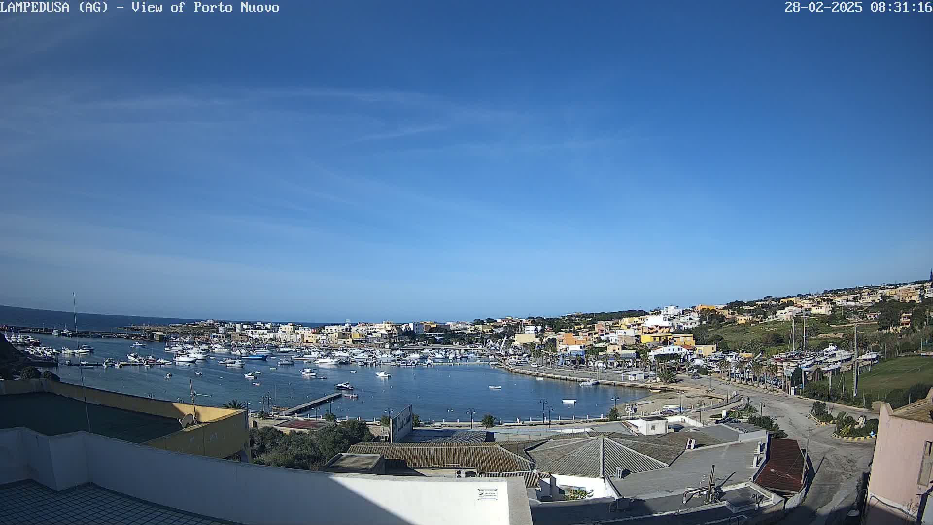 A harbor filled with boats is nestled in a town on a sunny day, with clear blue skies and calm water.