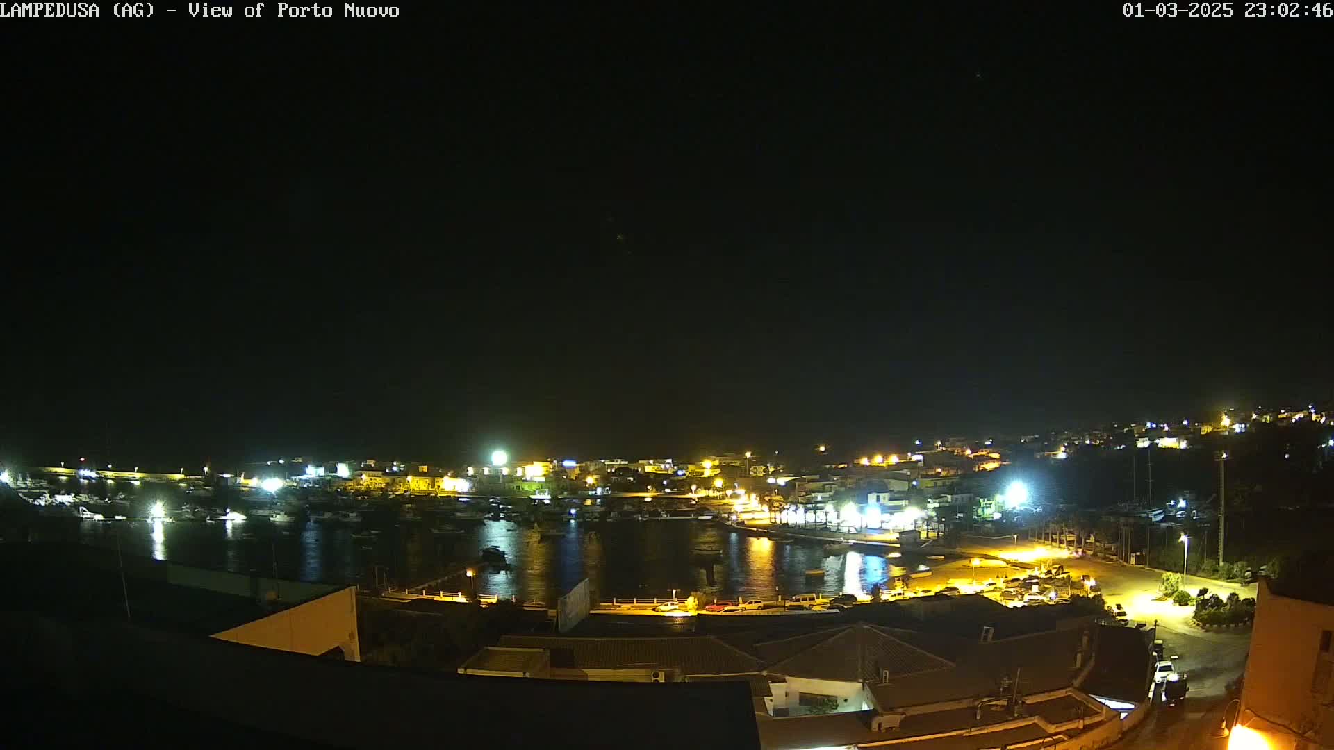 A nighttime, aerial view of a harbor town with many lights illuminating boats and buildings under a clear, dark sky.