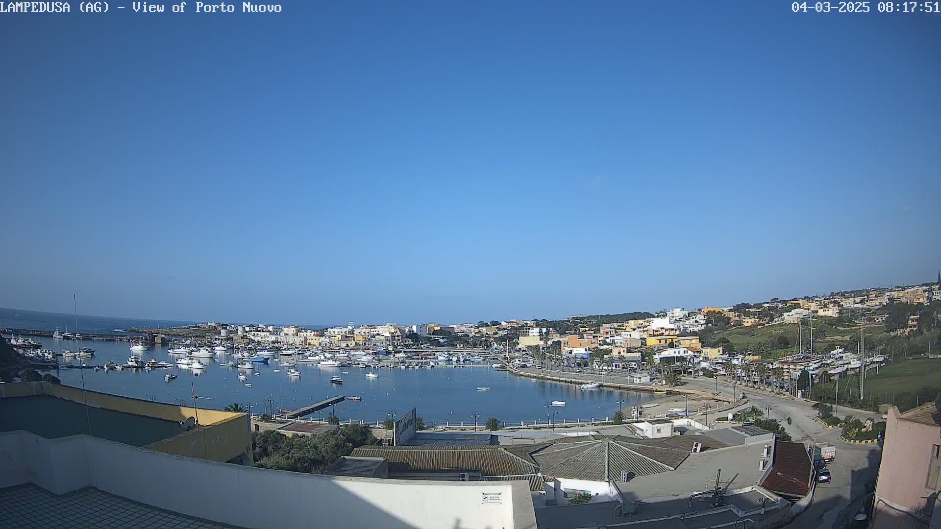 A clear, sunny day overlooks a harbor filled with boats and a town of low-rise buildings nestled along the coast.