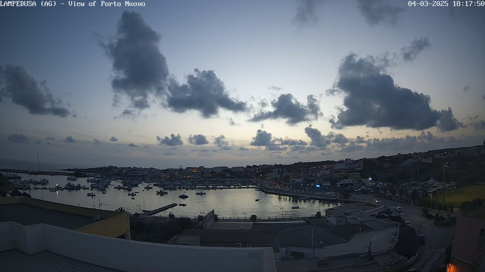 A harbor filled with boats is seen at dusk under a cloudy sky.