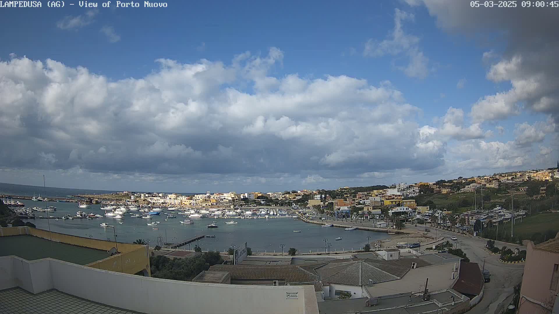 A harbor filled with boats is nestled in a town under a partly cloudy sky.