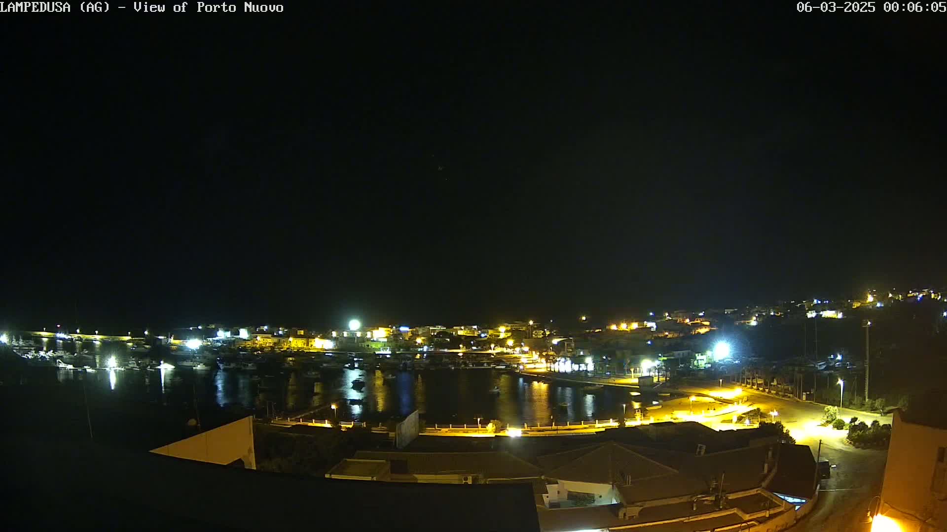 A nighttime, clear-weather view of a harbor filled with boats, surrounded by illuminated buildings and streets.