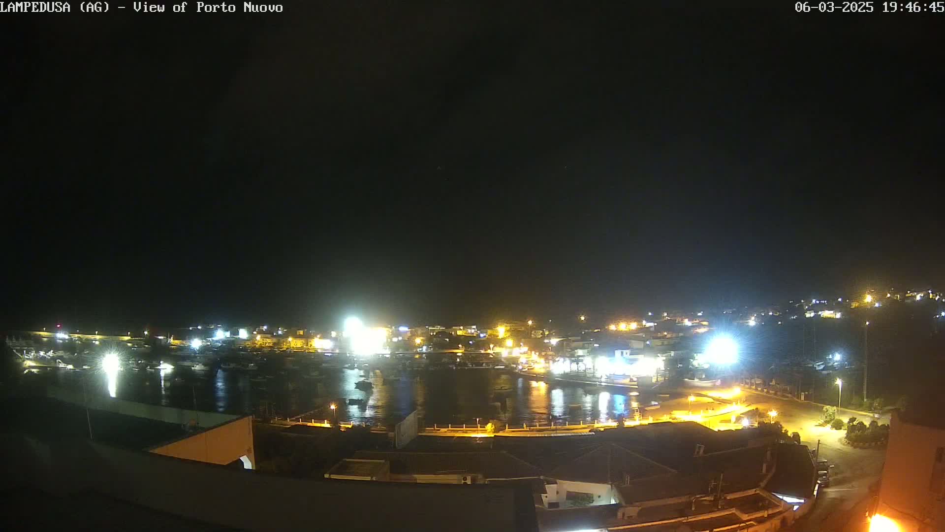 A nighttime, aerial view of a harbor filled with boats, surrounded by brightly lit buildings and streets.