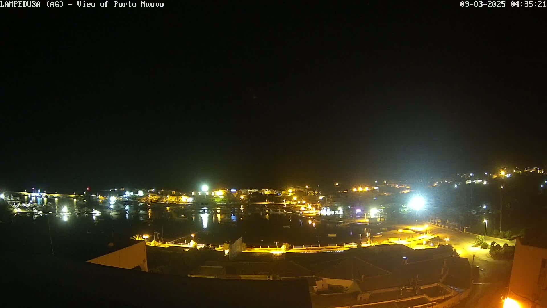 A nighttime, high-angle view of a harbor filled with boats, surrounded by illuminated buildings and streets.