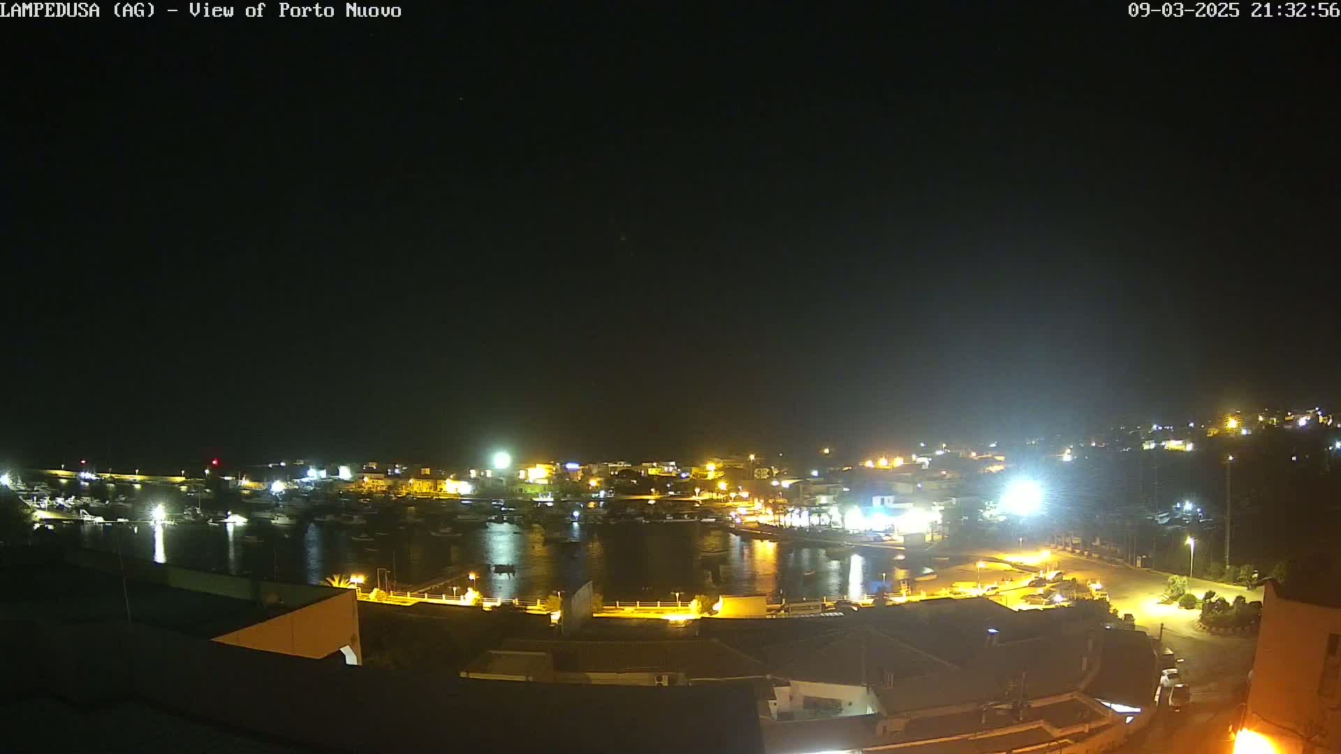 A nighttime view of a harbor filled with boats, surrounded by illuminated buildings and a dark sky.