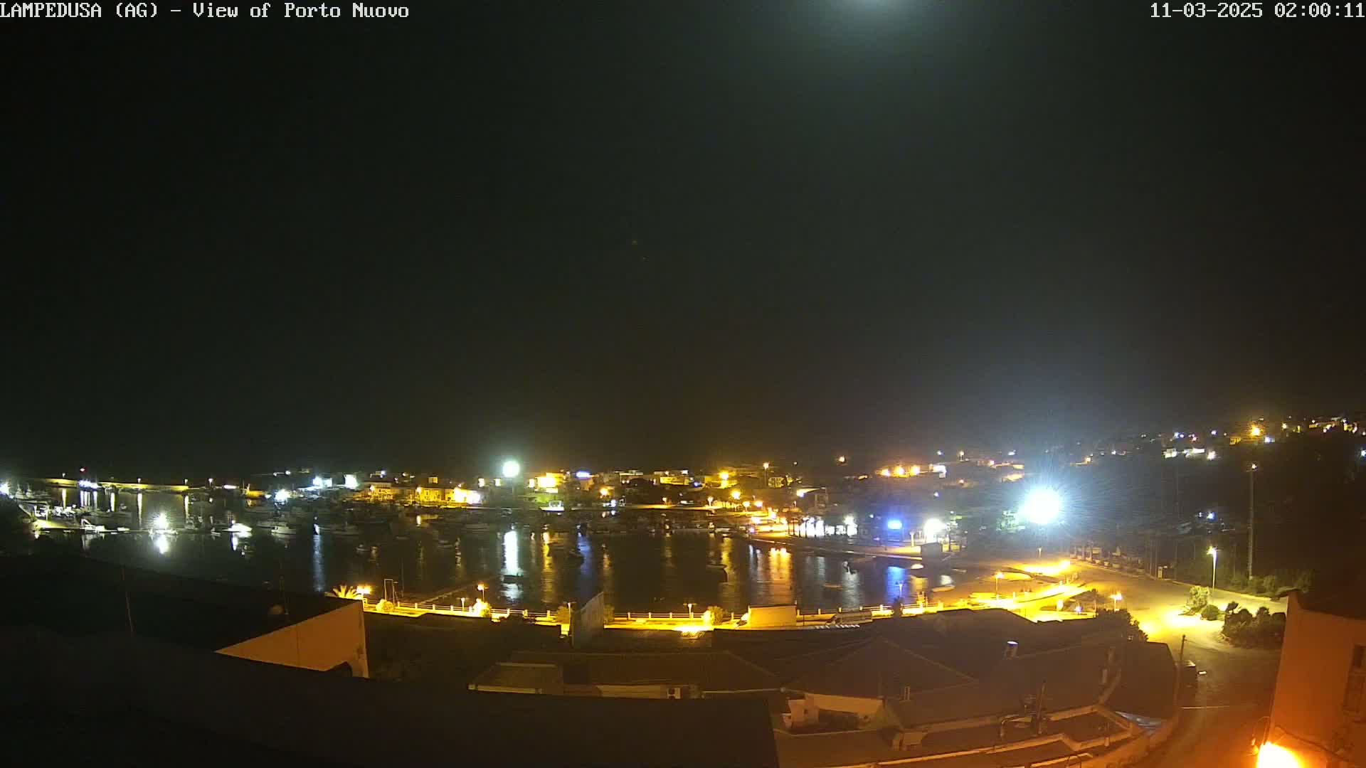 A nighttime, clear-sky view of a harbor filled with boats, surrounded by illuminated buildings and streets.