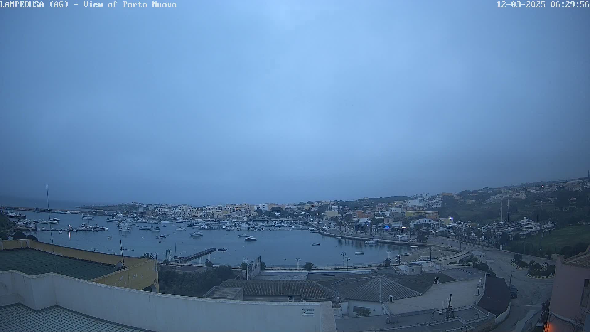 A harbor filled with boats is seen at dawn under an overcast sky.