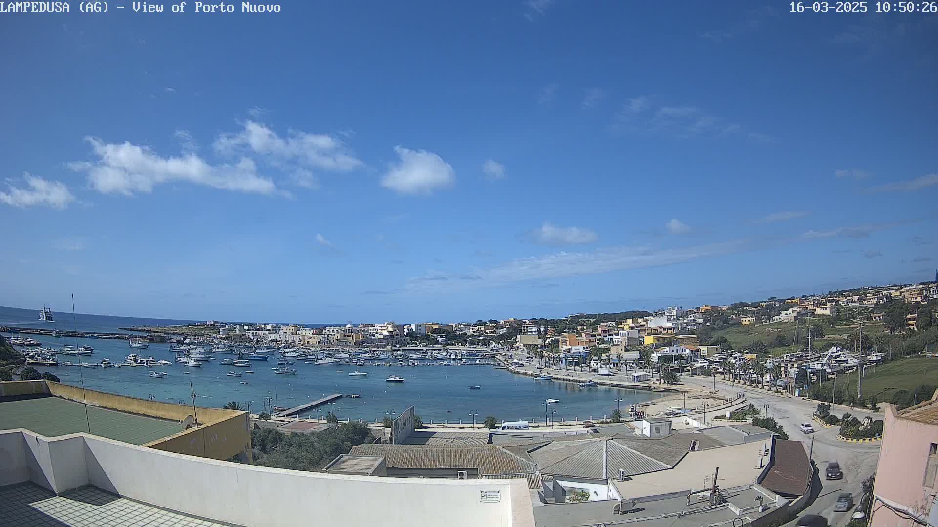 A mostly sunny day overlooks a harbor filled with boats and a town built on a hillside.