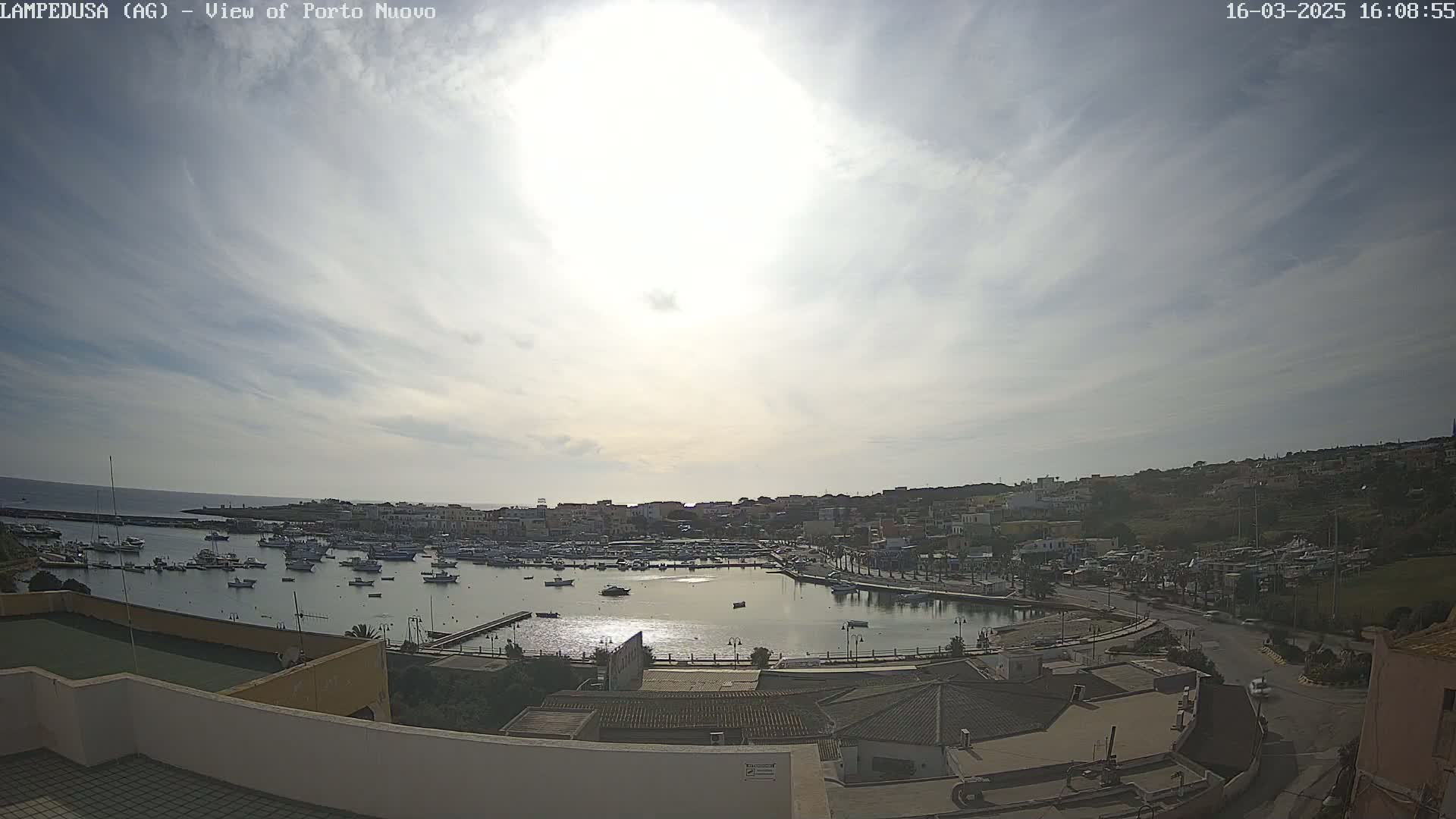 A harbor filled with boats is situated below a mostly sunny sky with scattered clouds.