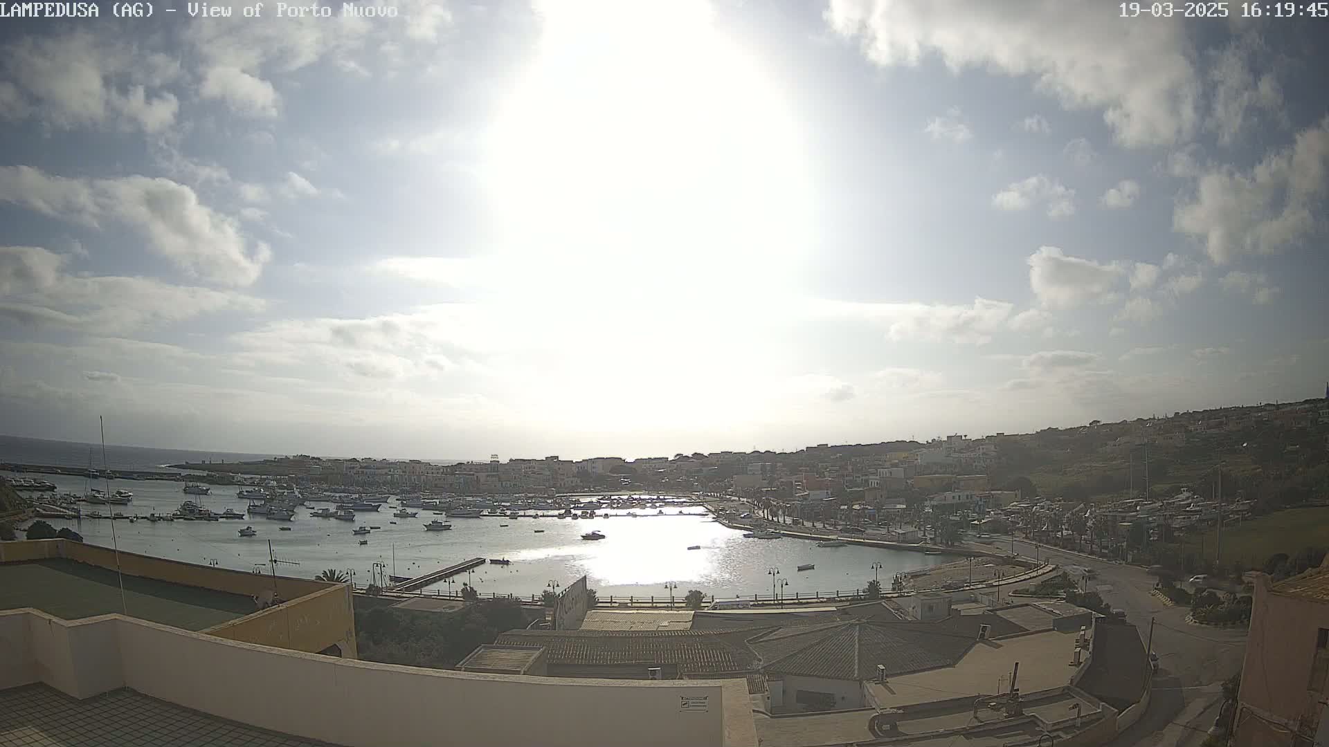A partly sunny day overlooks a harbor filled with boats and a town situated on a hillside.