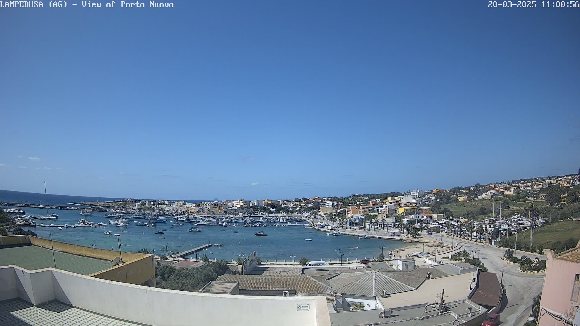 A harbor filled with boats is nestled in a town with low-rise buildings under a clear blue sky.