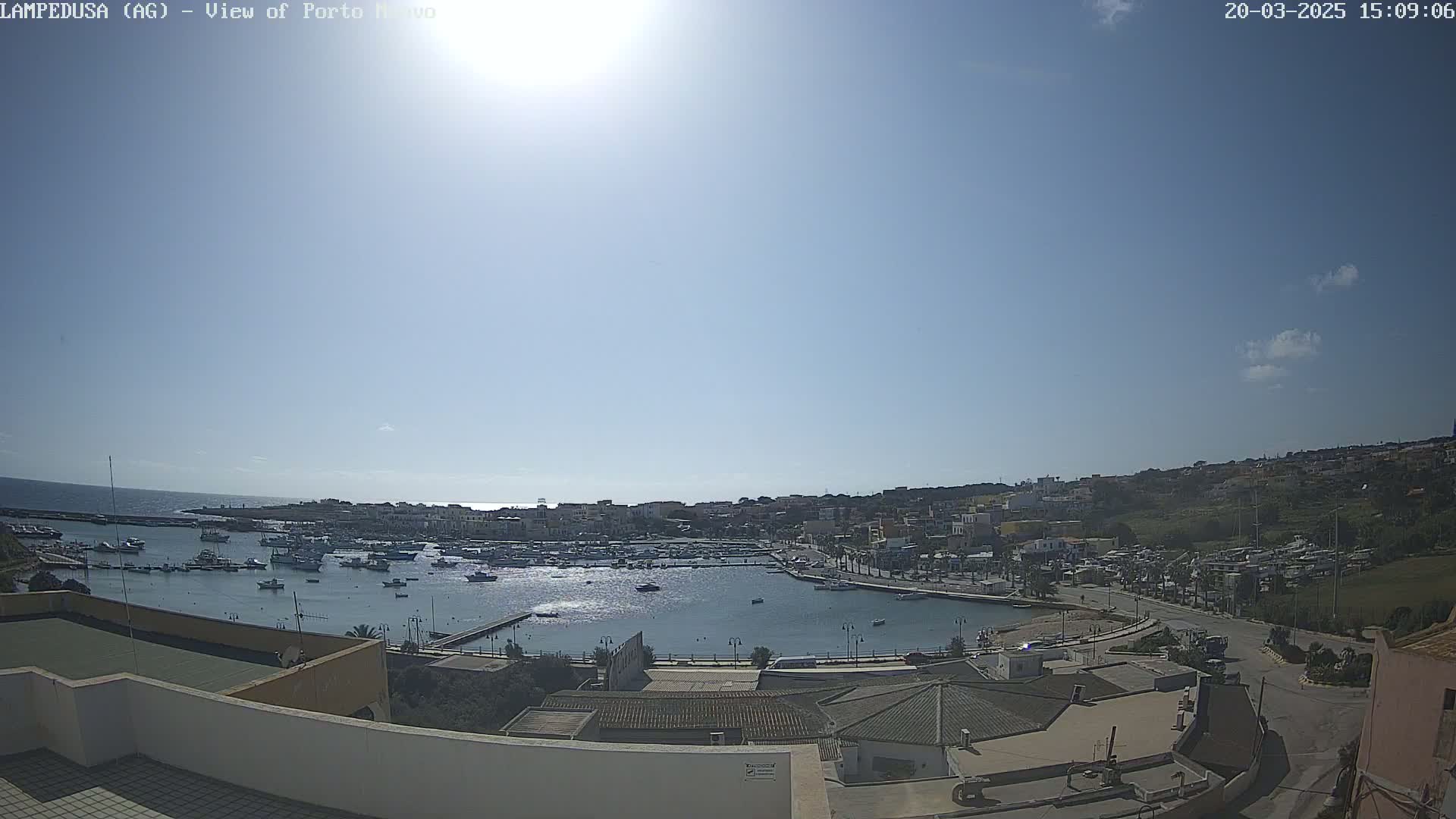 A sunny day overlooking a harbor filled with boats and a town situated on a hillside next to the ocean.