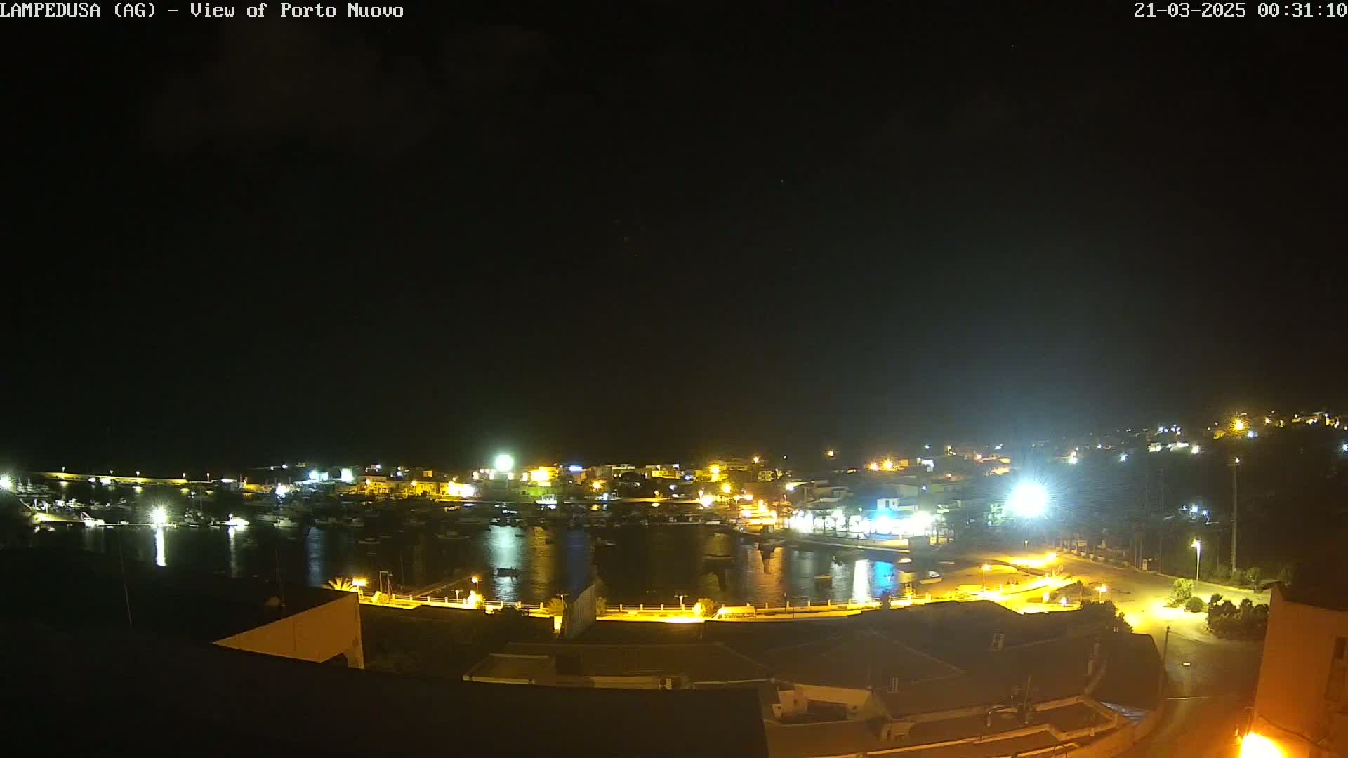 A nighttime, high-angle view of a harbor town, illuminated by many lights, under a clear, dark sky.