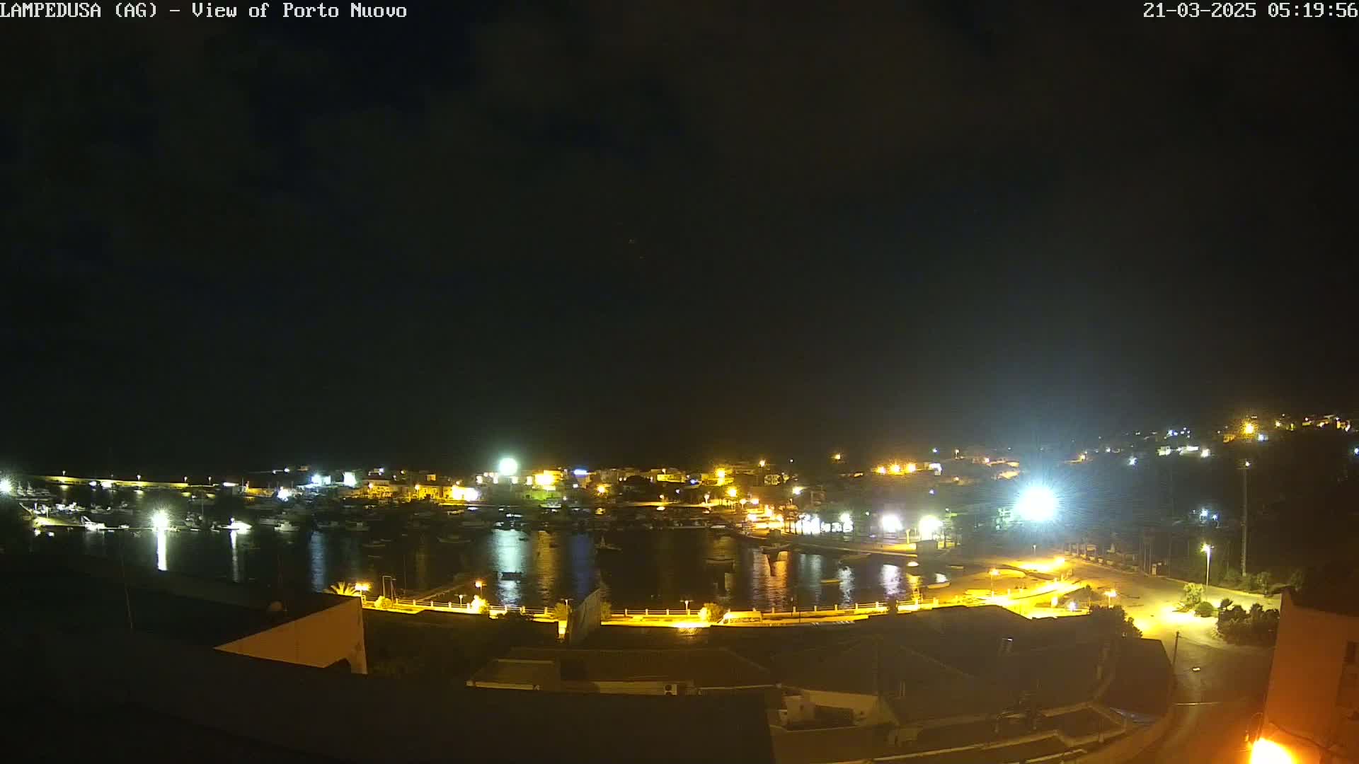 A nighttime, aerial view of a harbor filled with boats, surrounded by illuminated buildings on a clear night.