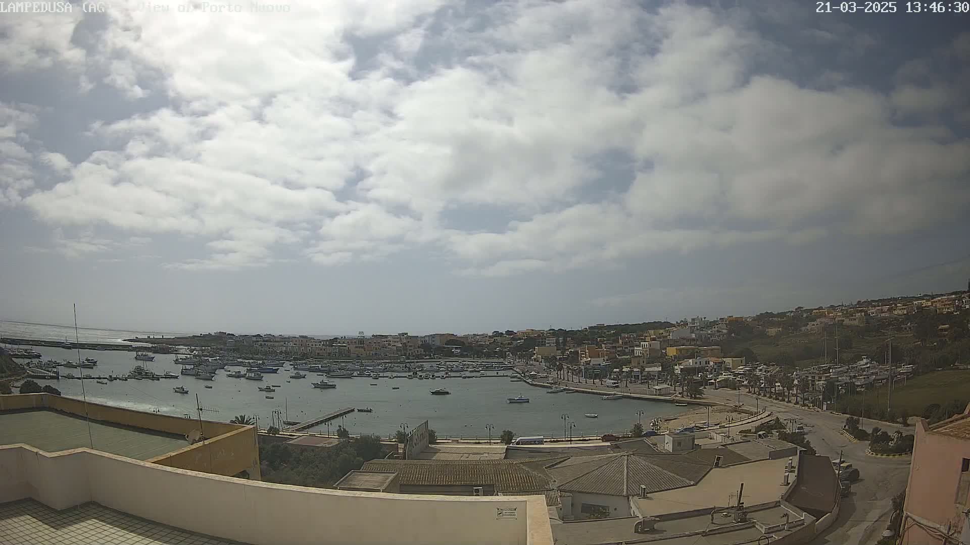 A partly cloudy day overlooks a harbor filled with boats and a town built on a hillside.