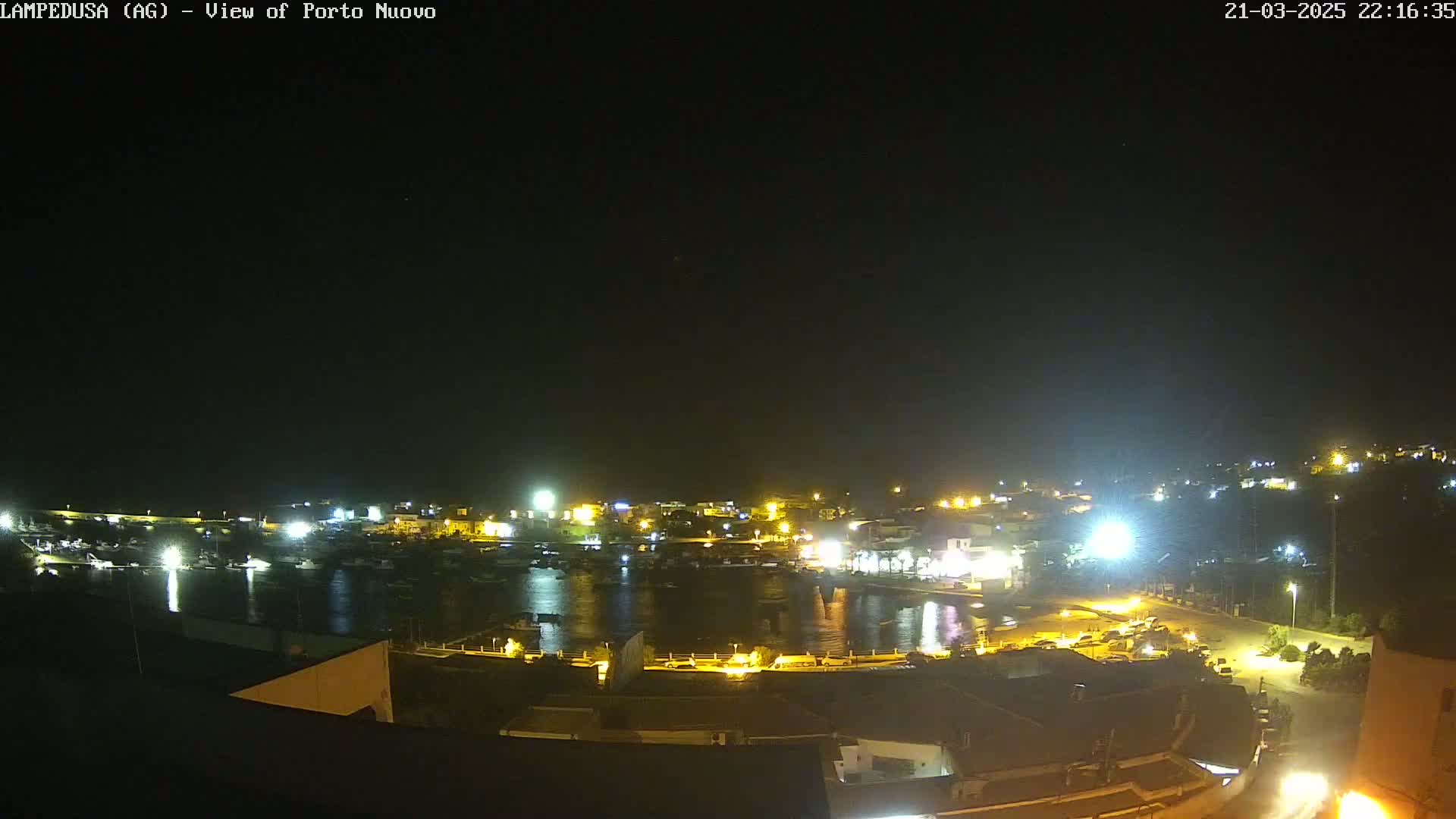A nighttime view of a harbor filled with boats, surrounded by illuminated buildings and a dark sky.