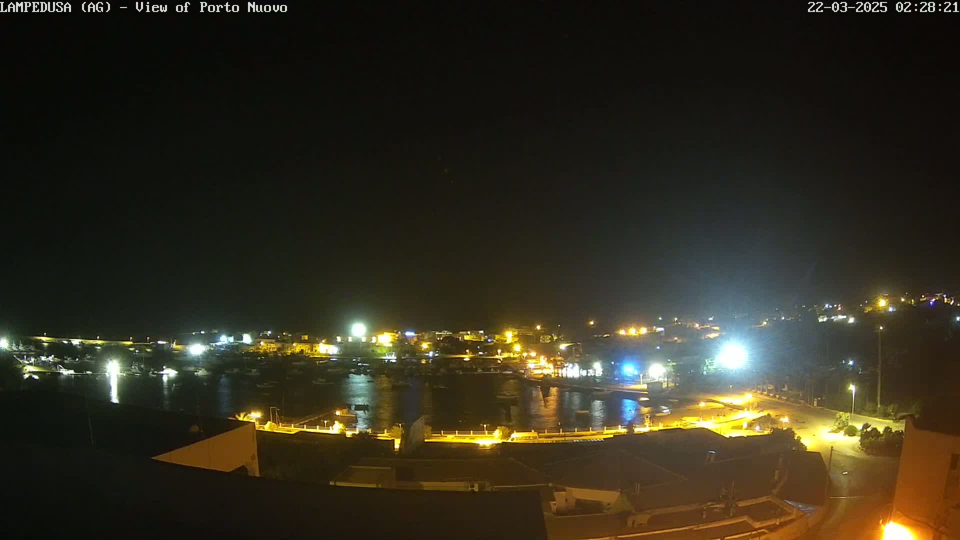 A nighttime view of a harbor filled with boats, surrounded by buildings with illuminated streets and lights.