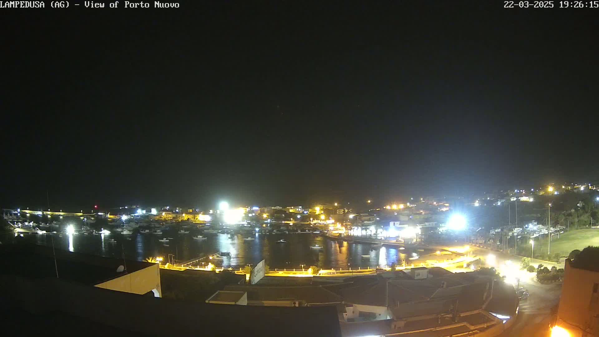 A nighttime, aerial view of a harbor filled with boats, surrounded by brightly lit buildings and roads.