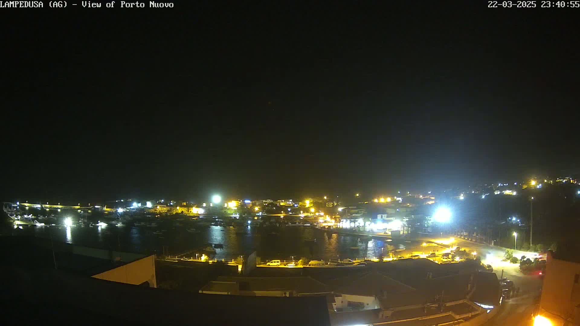 A nighttime, high-angle view of a harbor filled with boats, surrounded by illuminated buildings and streets.