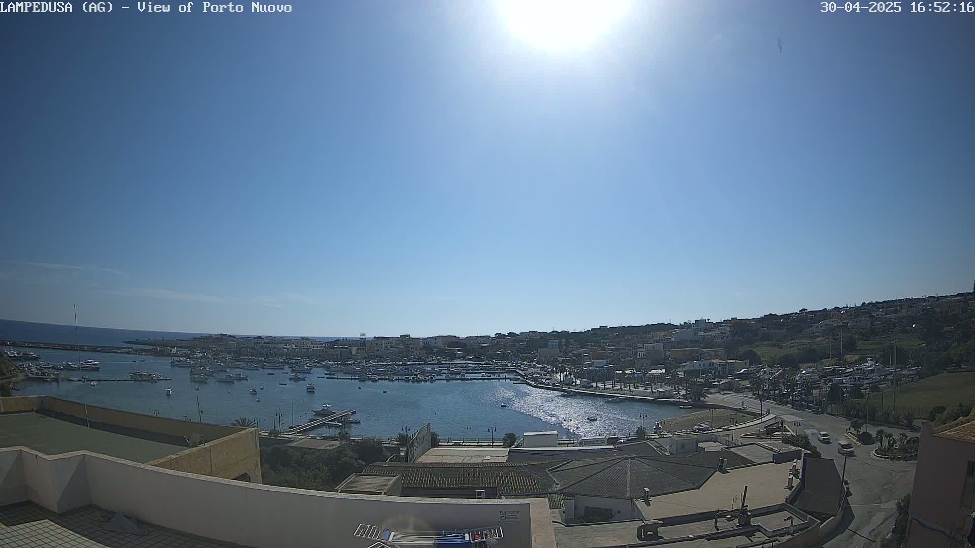 A sunny day reveals a harbor filled with boats, adjacent to a town built on a hillside overlooking the sea.