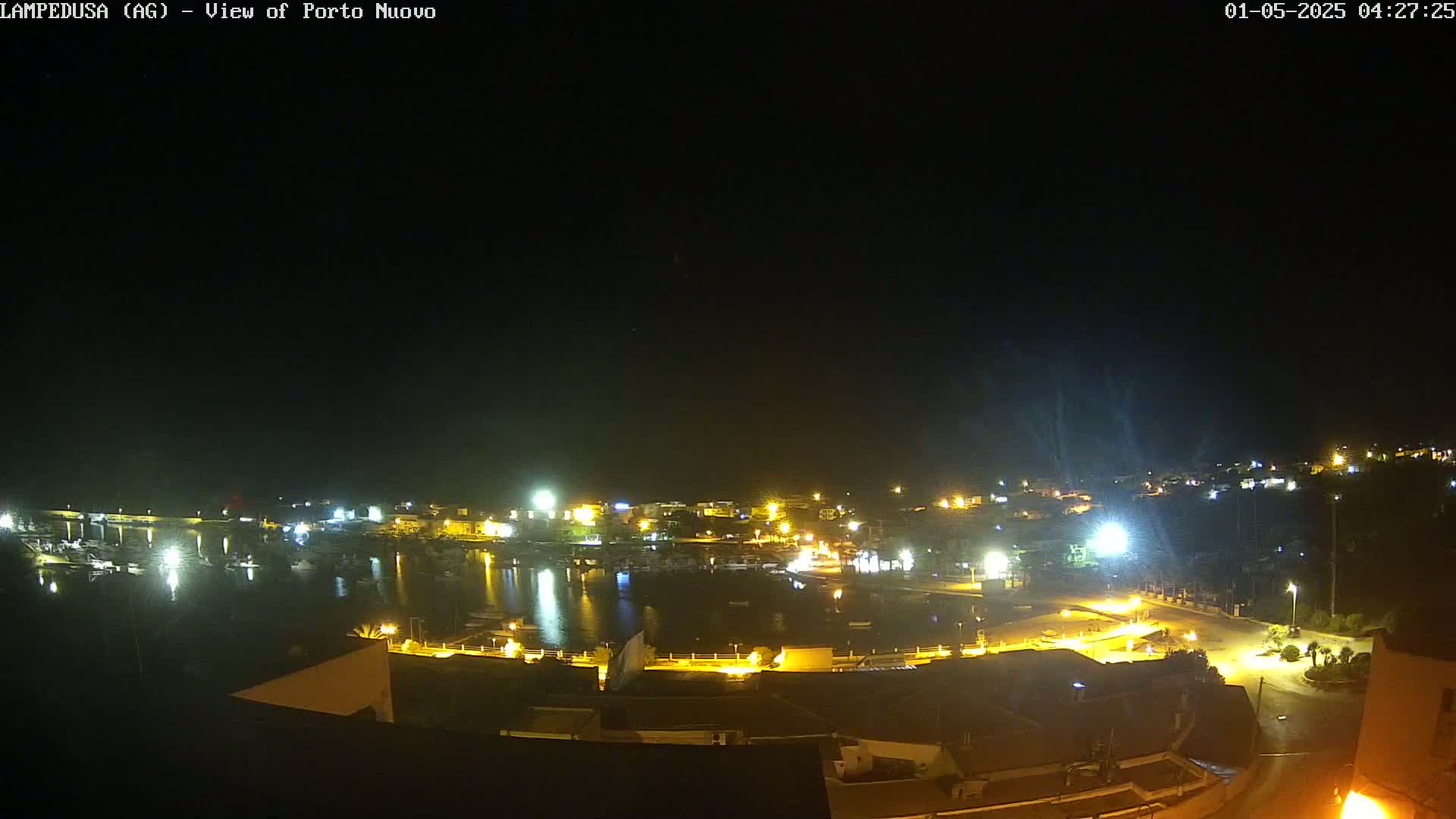 A nighttime aerial view of a harbor town with many lights illuminating the buildings and water.