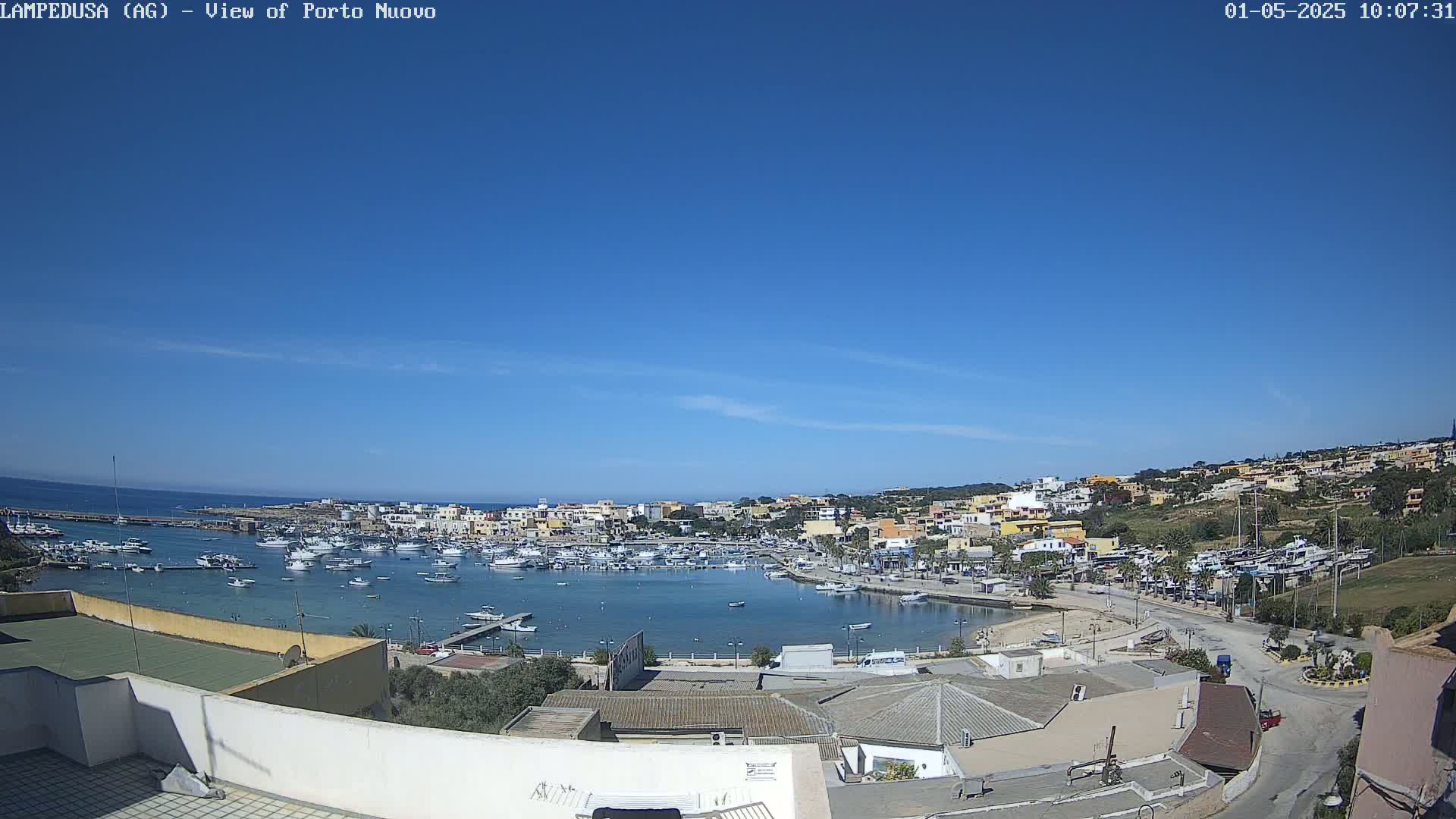 A harbor filled with boats is nestled in a town of low-rise buildings under a clear blue sky.