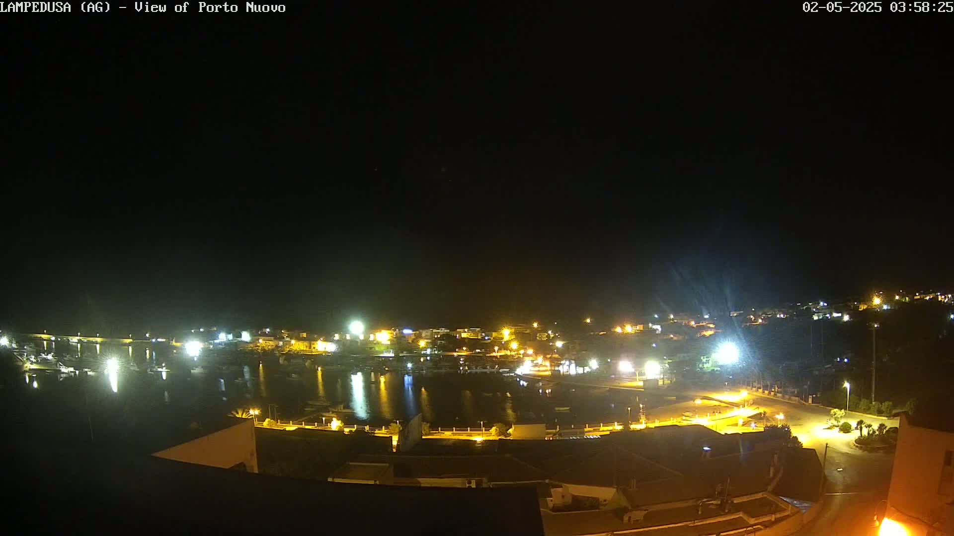 A nighttime view of a harbor town illuminated by many lights under a clear, dark sky.