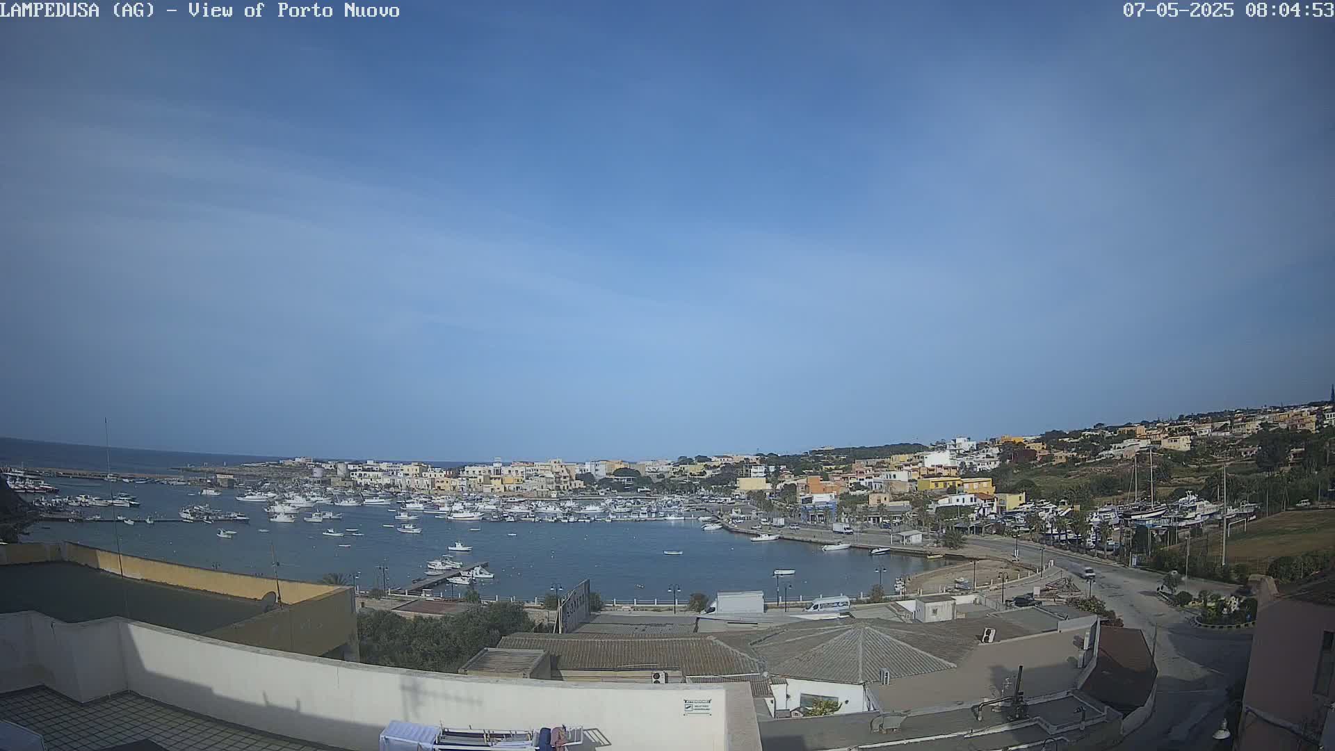 A clear, sunny day overlooks a harbor filled with boats, surrounded by a town of low-rise buildings.