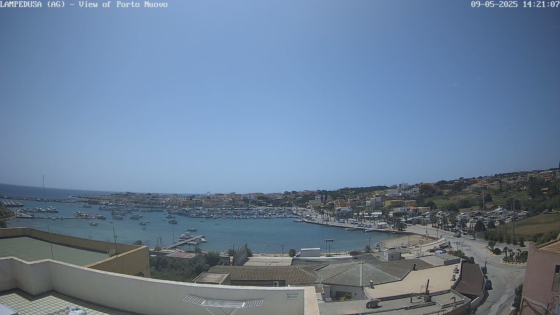 A harbor filled with boats is nestled into a town on a sunny day, with a clear blue sky above.
