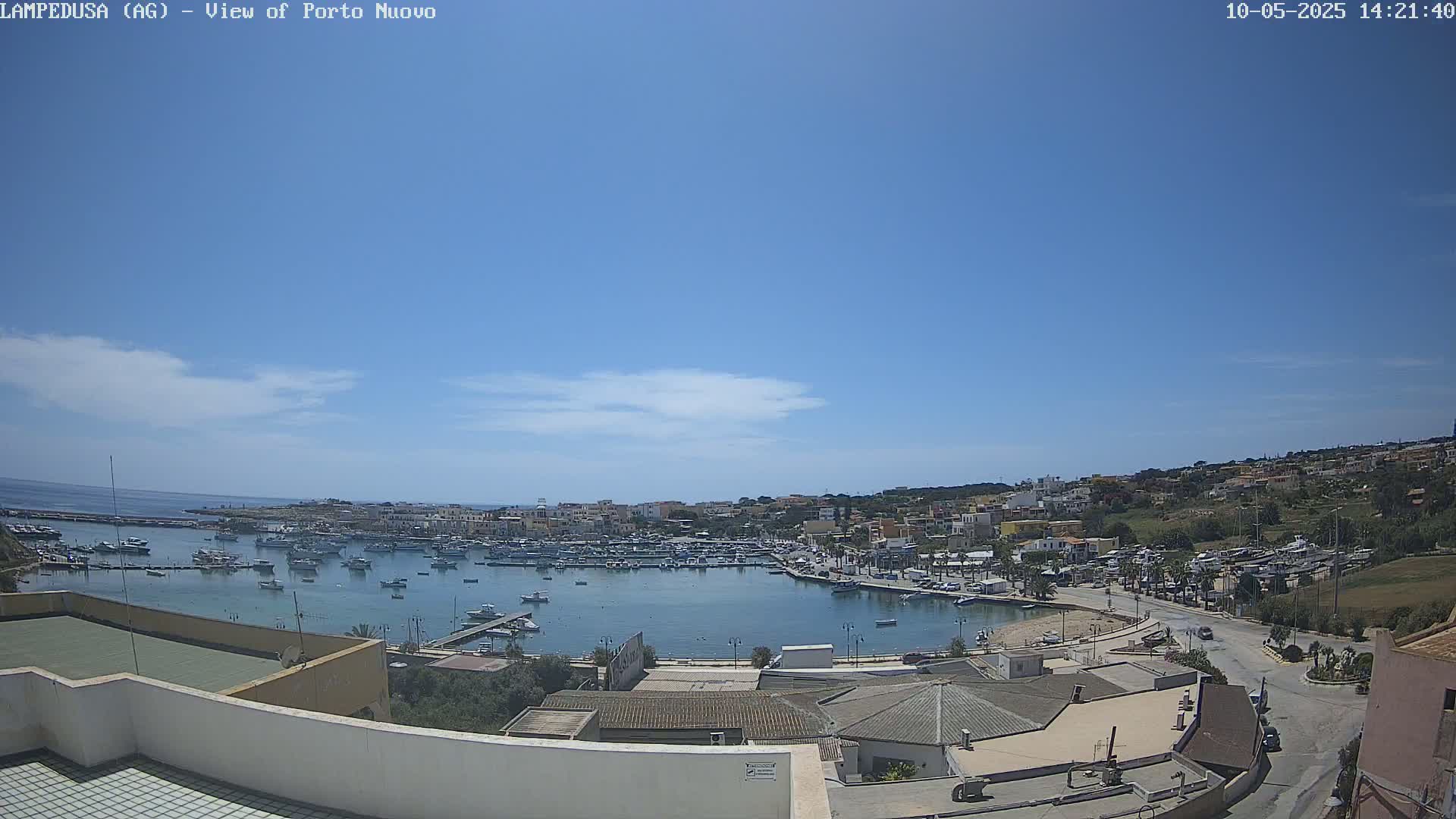 A harbor filled with boats is nestled in a town under a clear, bright blue sky with a few wispy clouds.