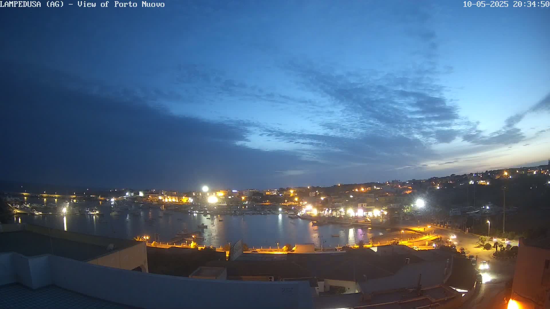 A nighttime view of a harbor town, illuminated with lights under a twilight sky with mostly clear skies.