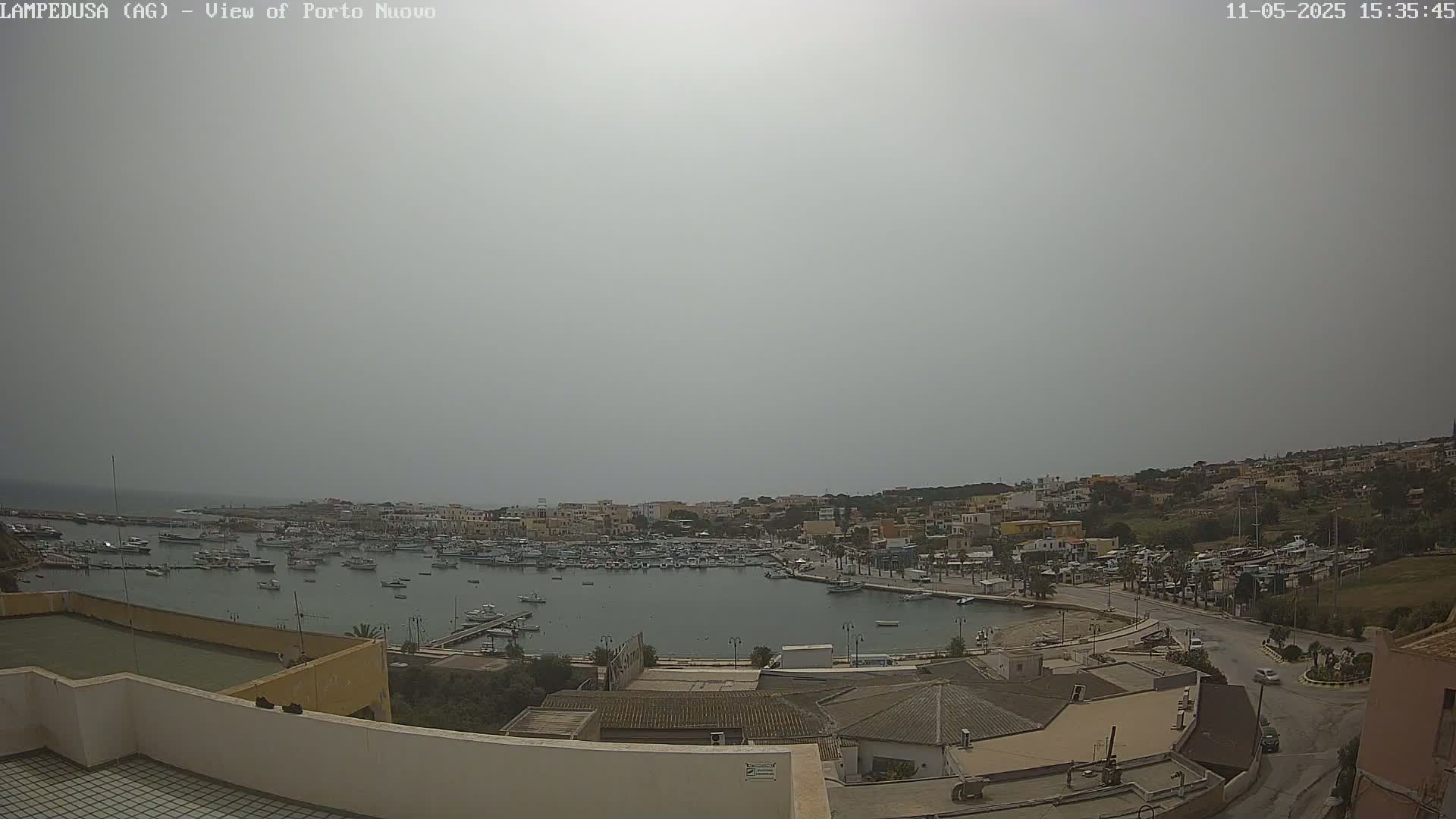 A hazy view of a harbor filled with boats, surrounded by a town on a hill.