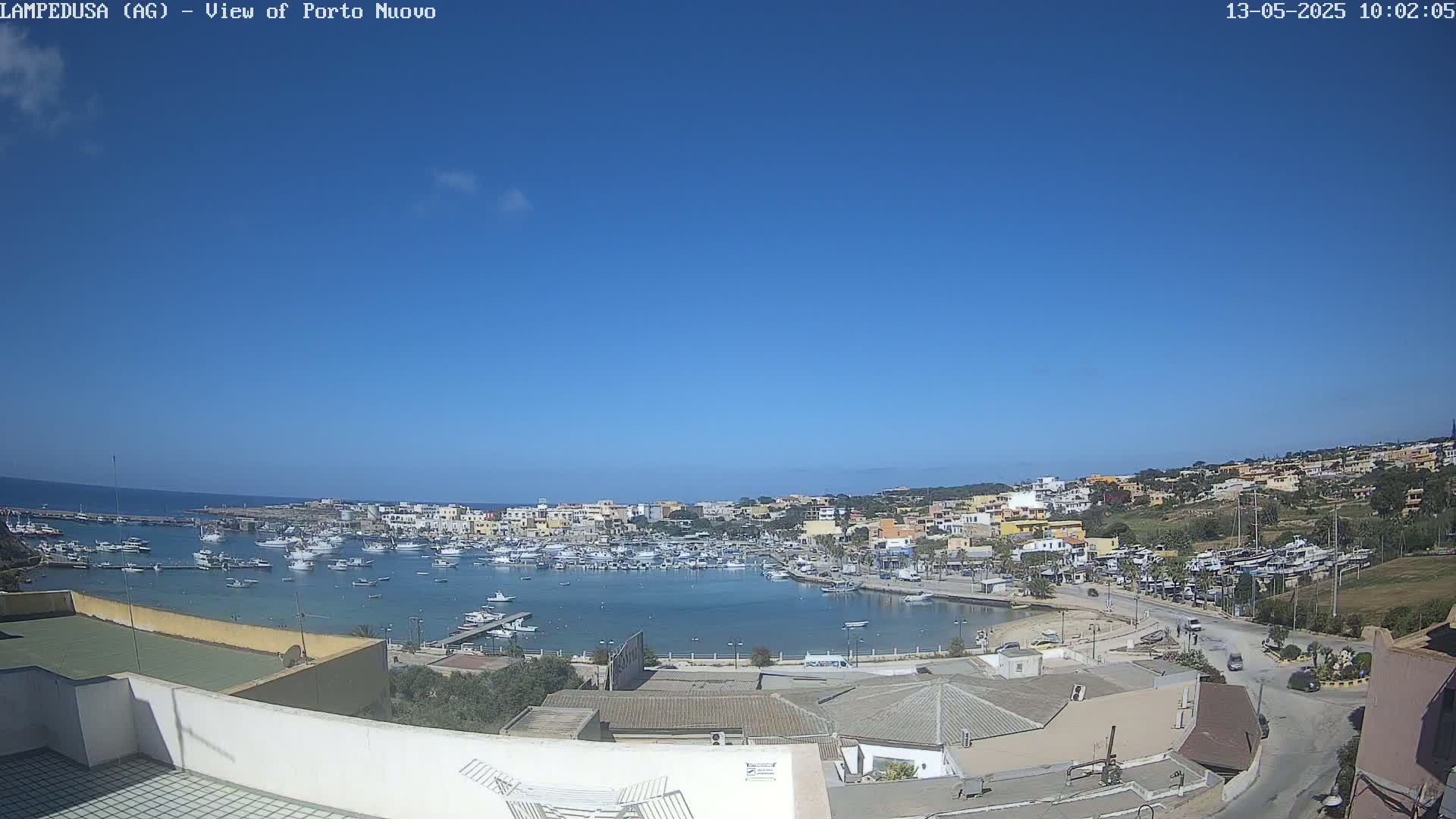A harbor filled with boats is situated in a town on a sunny day with a clear blue sky.