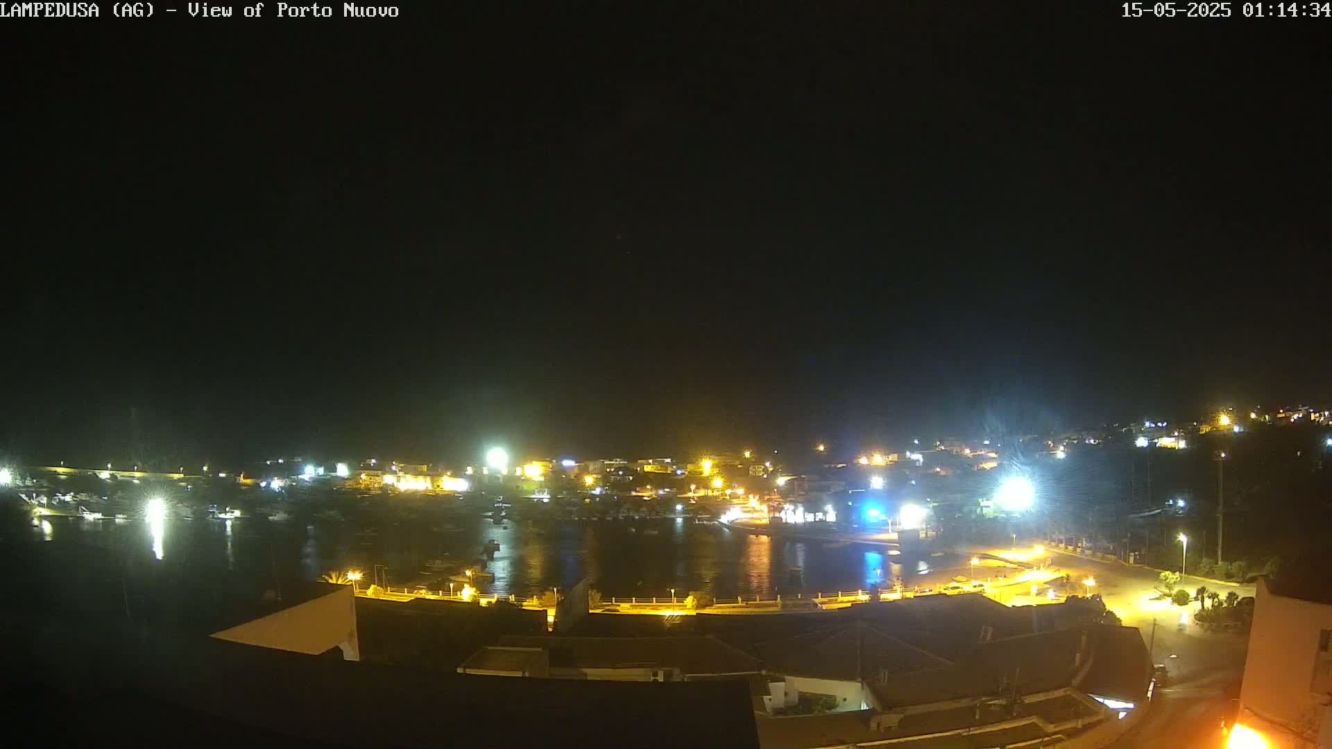 A nighttime view of a harbor town illuminated by lights, with calm water reflecting the lights.