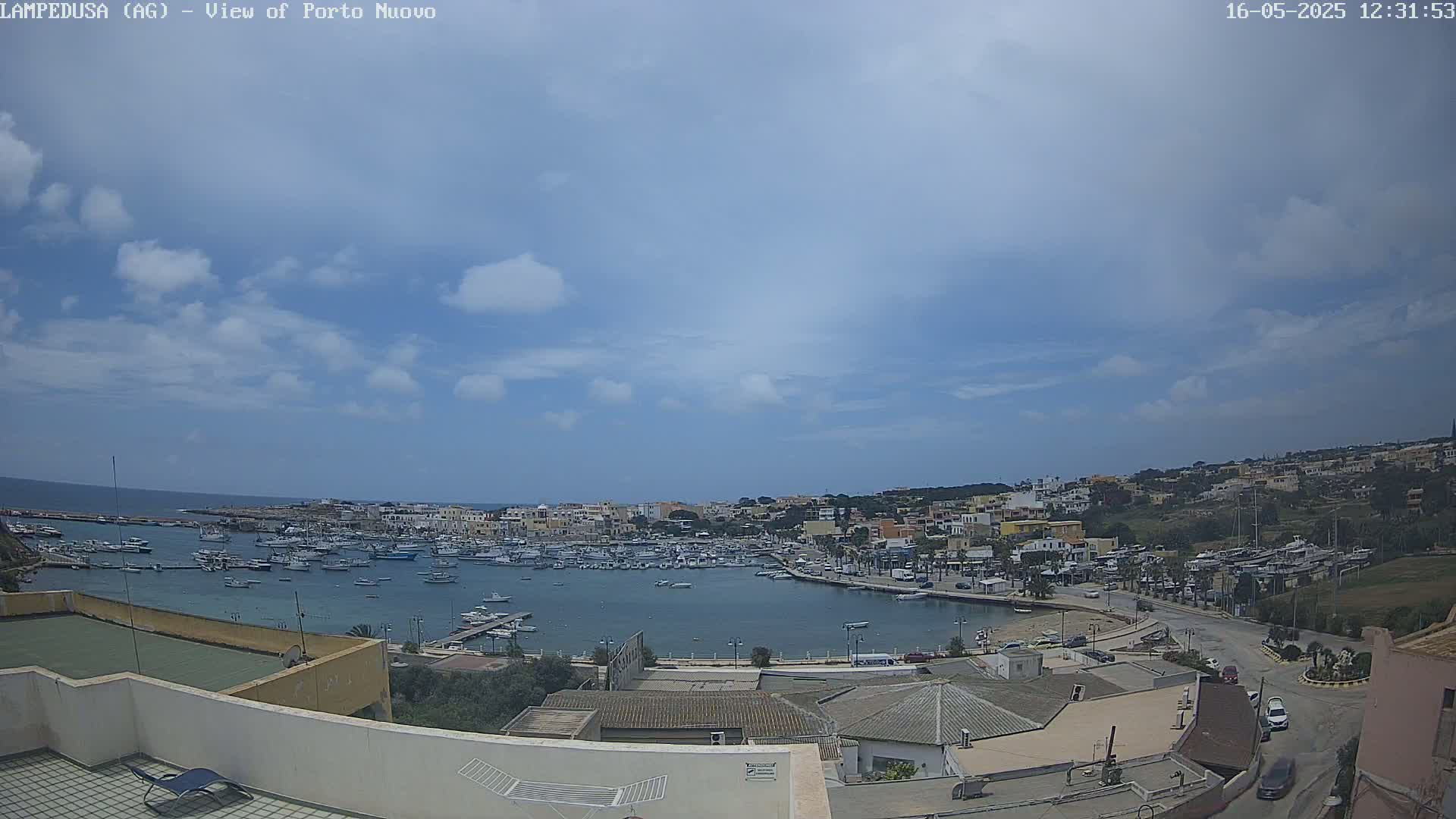 A partly cloudy day overlooking a harbor filled with boats and a town built on a hillside.