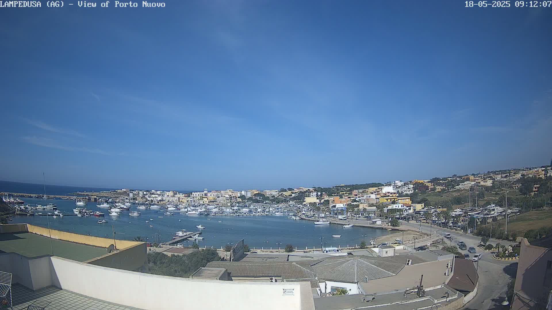 A harbor filled with boats is surrounded by a town of low-rise buildings under a clear blue sky.
